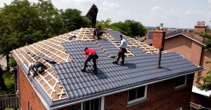 Workers installing a new grey metal roof on a two-storey brick home
