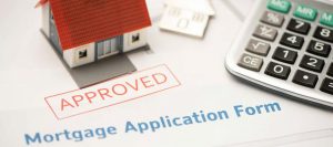 Miniature house model with red roof beside a calculator, sitting on an approved mortgage application form