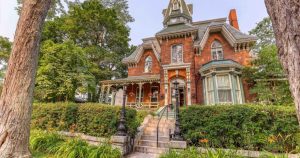 Front view of the Hochelaga Inn, a 19th-century red brick Victorian mansion with ornate trim, bay windows, and lush gardens in Kingston’s Sydenham Ward.