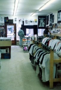Interior of Vinyl Vendor record store on Princess Street in 1990, with racks of T-shirts, posters, and records; Bill Stevenson visible at the counter.