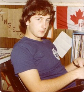 Bill Stevenson in his Gore Street apartment in 1977, wearing a Morris Hall shirt with a Canadian flag and records in the background.