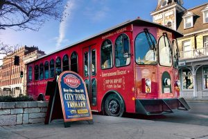 Red Kingston City Tour Trolley parked downtown with signboard for hop-on hop-off tours.