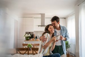 A smiling young couple embraces while holding coffee mugs in a bright modern kitchen, symbolizing the excitement of first-time home buyers in Kingston, Ontario.