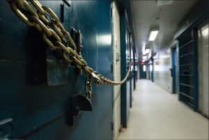 A chained and padlocked cell door inside Kingston Penitentiary, with a view down the corridor of heavy steel doors and barred gates.