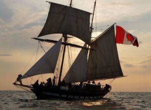 The St. Lawrence II tall ship sailing on Lake Ontario at sunset with the Canadian flag flying.