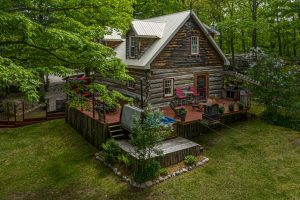 Country home with log siding, landscaped yard, and outdoor deck seating, showing curb appeal in a rural setting.