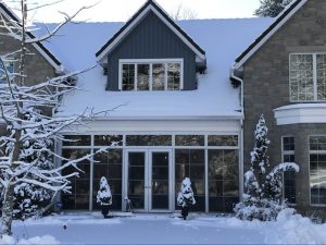Front of a home in winter with snow-covered roof and landscaping, showing how clear paths and evergreens enhance curb appeal.