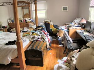 A cluttered bedroom filled with clothes, papers, and household items before decluttering, shown as part of Century 21 Lanthorn Real Estate downsizing tips