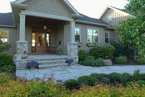 Front entry of a home with stone steps, wood door, and landscaped garden beds, showing inviting curb appeal.