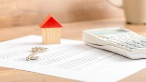 Keys, calculator, and house model resting on a real estate contract representing home sale offers