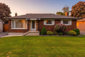 Brick bungalow in Kingston’s west end at dusk, surrounded by mature trees and soft light, symbolizing calm transitions for families selling their homes. Bill Stevenson, REALTOR®, Century 21 Lanthorn Real Estate Ltd., Brokerage.