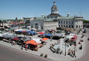 Kingston Public Market in Market Square with vendors and shoppers in front of City Hall on a summer day.