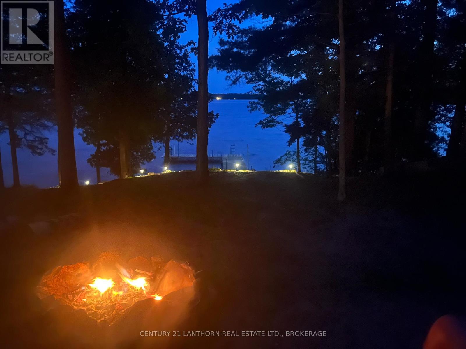 Evening waterfront firepit overlooking Sharbot Lake with dock lights and wooded shoreline setting