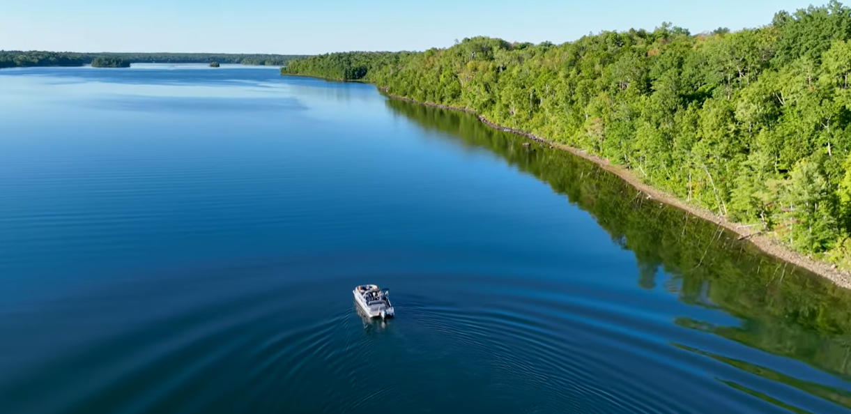 Boat travelling across a large lake surrounded by forest in South Frontenac near Kingston Ontario