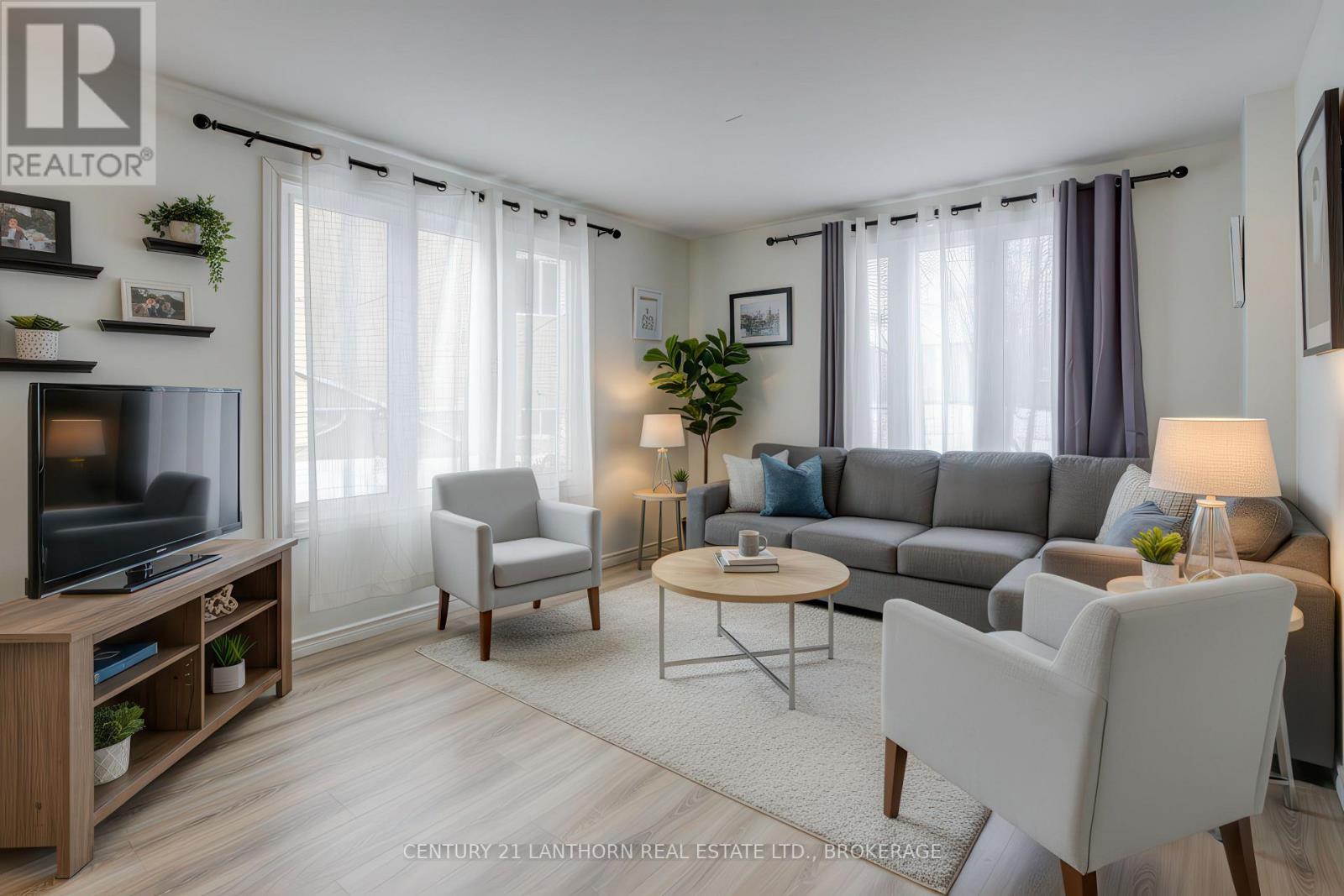 Living room at 6 Woodstone Crescent in Kingston featuring large windows, updated flooring, and virtually staged furnishings. Bill Stevenson, REALTOR®, Century 21 Lanthorn Real Estate Ltd., Brokerage.