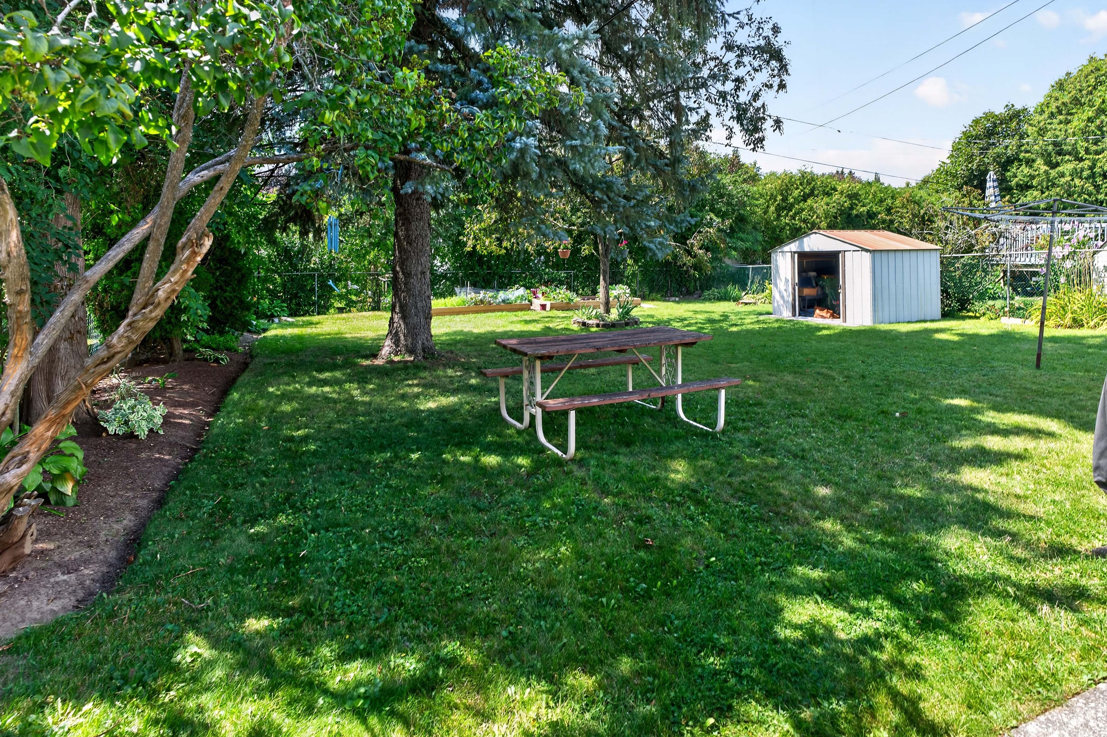 Fully fenced backyard at 742 Laidlaw Crescent Kingston with mature trees, garden beds, lawn, and storage shed